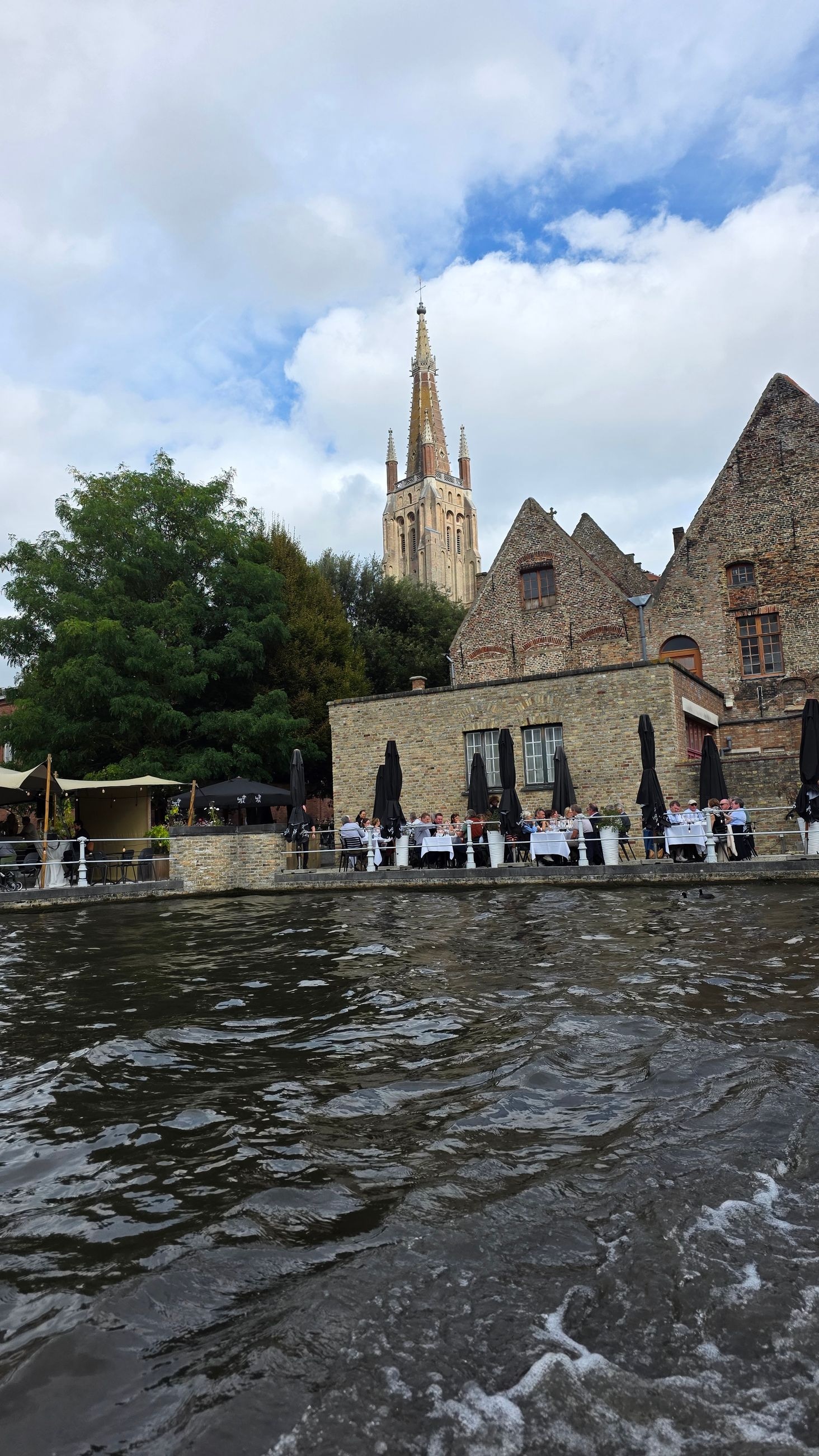 View from a canal boat, Church of Our Lady's spire rising above a canalside restaurant terrace