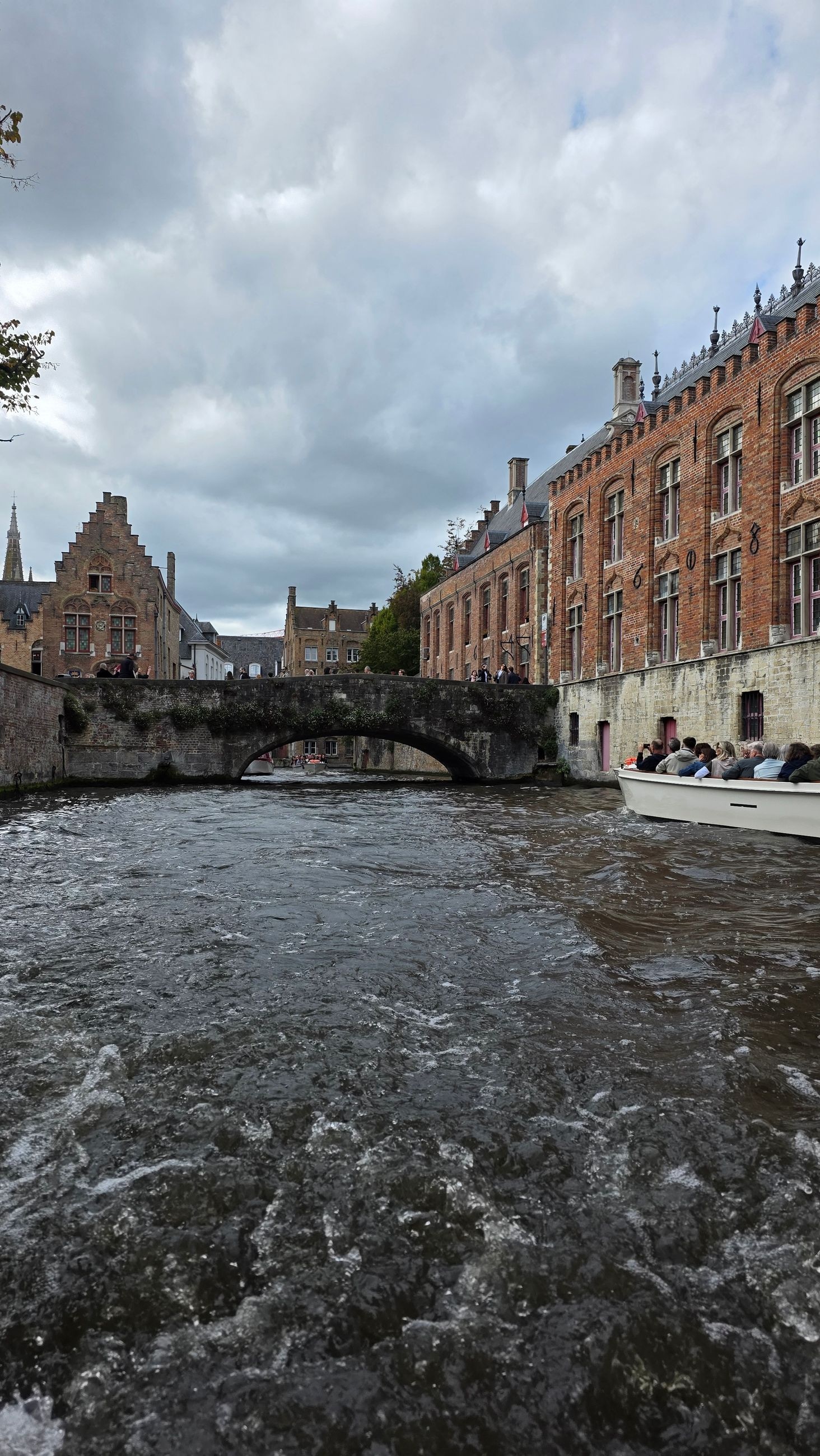 View from a canal boat passing under a stone bridge, Church of Our Lady's spire in the background