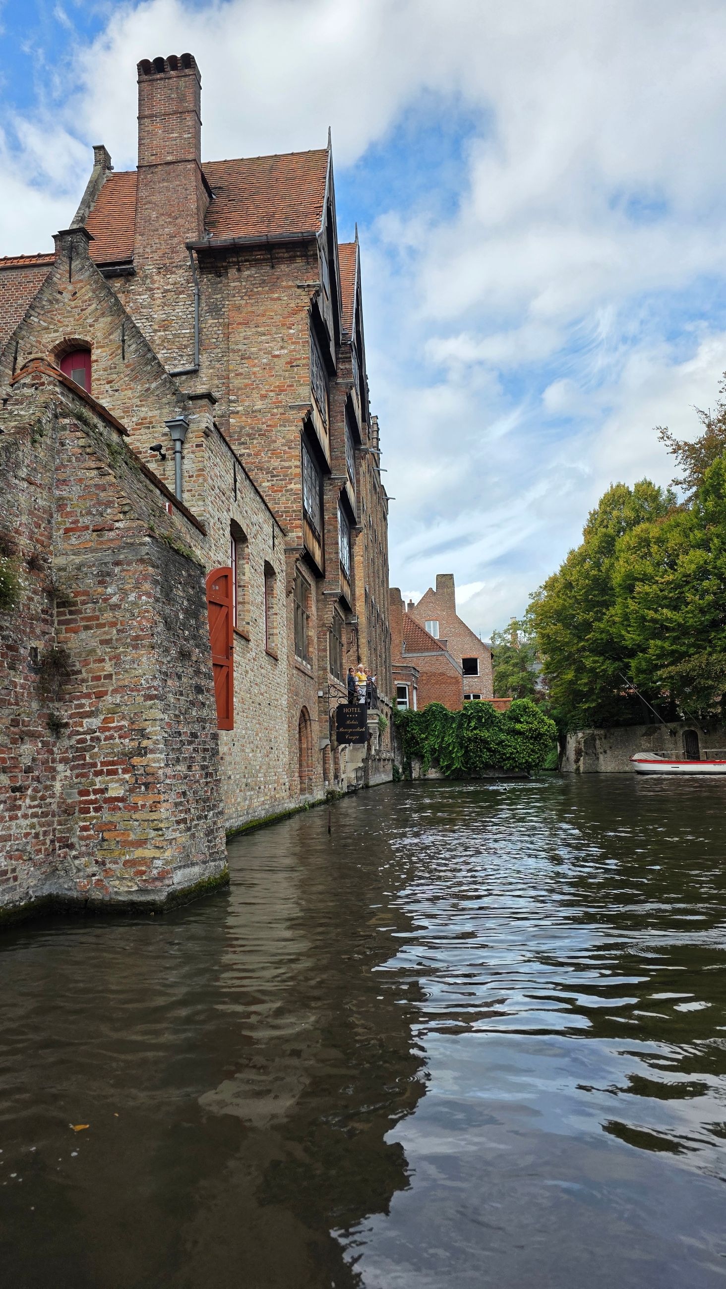 An old brick canal house with red window shutters along a narrow Bruges canal