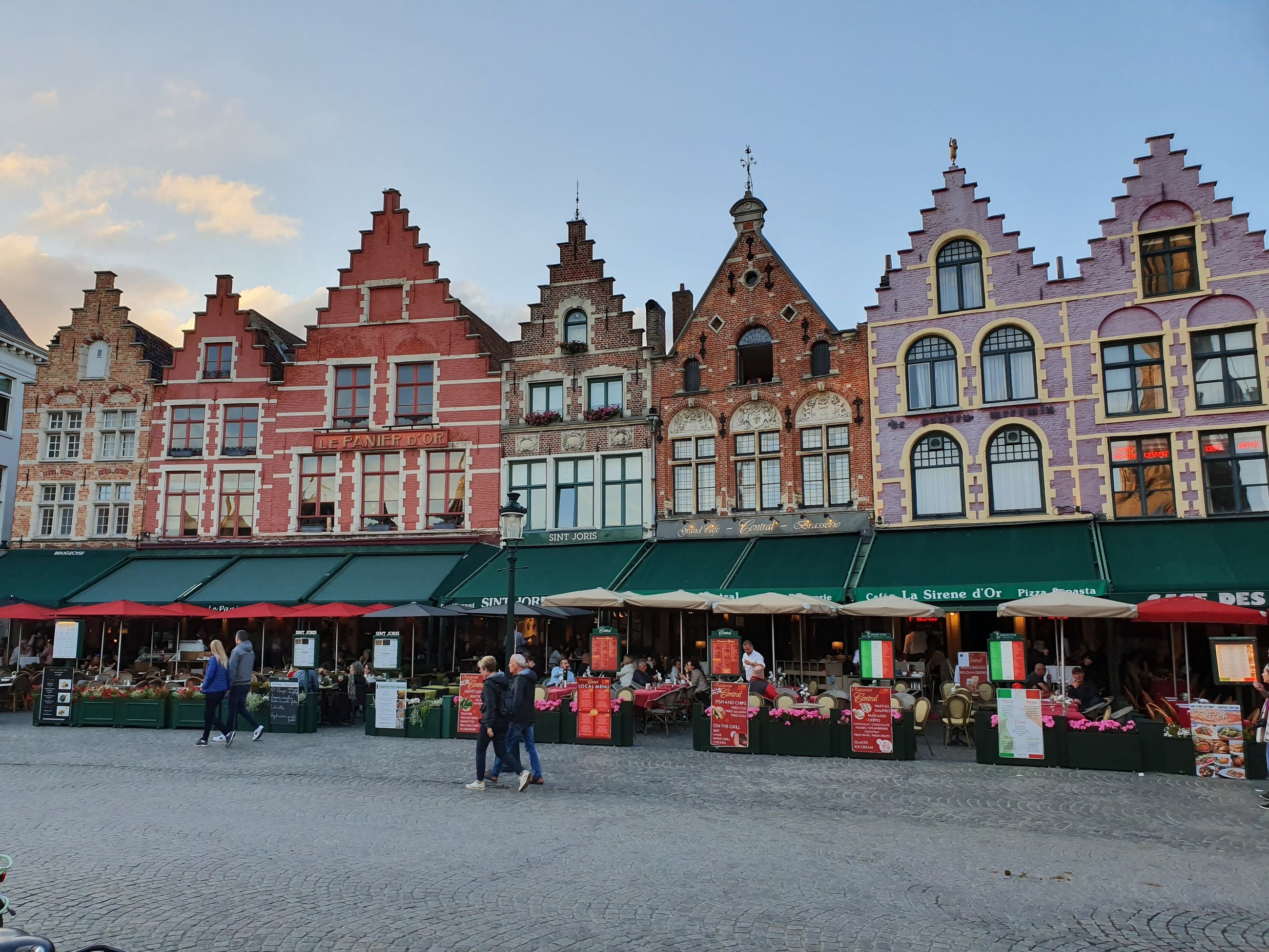 Colorful stepped-gable guild houses around Bruges' Markt square, with outdoor cafe terraces below