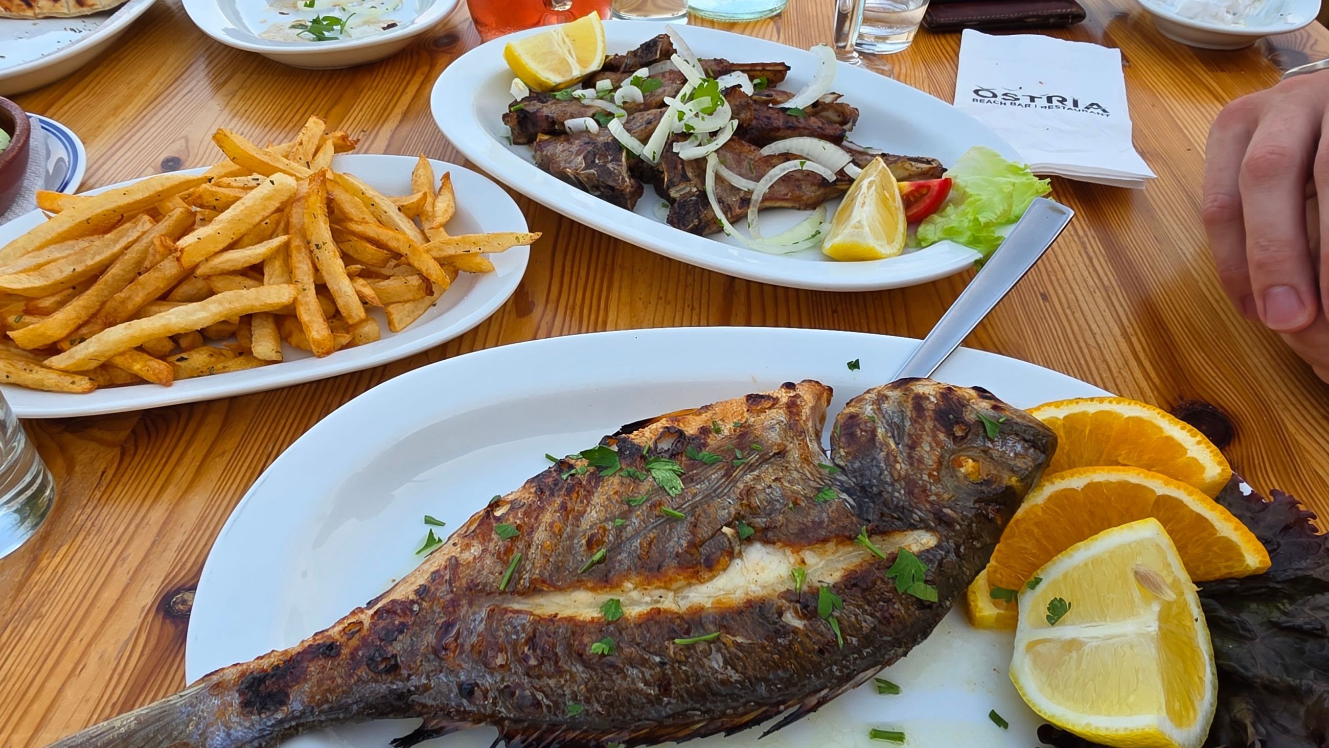 A table full of food from Osteria restaurant: grilled fish, lamb chops and fried fries